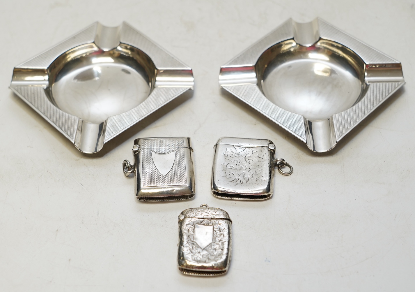 A pair of George V Asprey & Co silver ashtrays, 86mm and three assorted silver vesta cases. Condition - fair to poor.